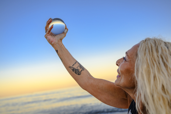 Nancy de YoSoy444 sosteniendo una esfera de cristal frente al mar para una sesión de Registros Akáshicos.
